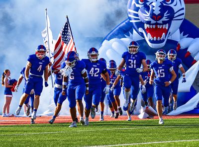 The Cougars run out of the Cougar tunnel carrying the American flag